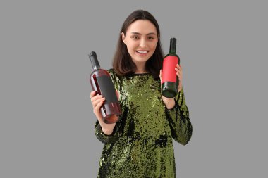 Gri arka planda şarap şişeleri olan güzel genç bir kadın.