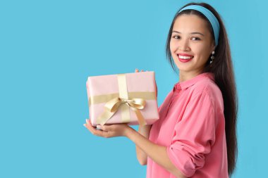 Mavi arka planda hediye kutusu olan güzel bir Asyalı kadın.