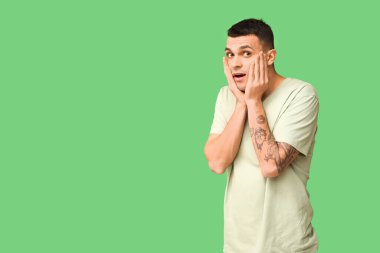 Handsome ashamed young man covering face with hands on green background clipart