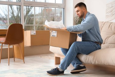 Evdeki kanepede paketleri açan genç adam.