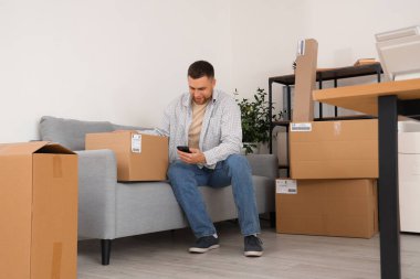 Depoda paketli ve cep telefonlu bir erkek satıcı oturuyor.