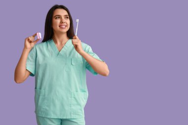 Diş fırçası ve mor arka planda plastik dişi olan kadın bir dişçi. Dünya Diş Hekimi Günü