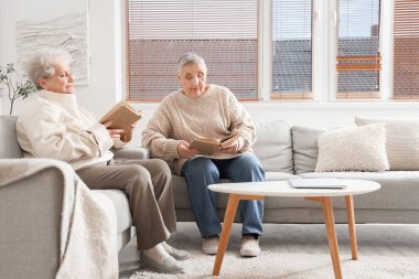 Evde kitap okuyan kıdemli bayan arkadaşlar.