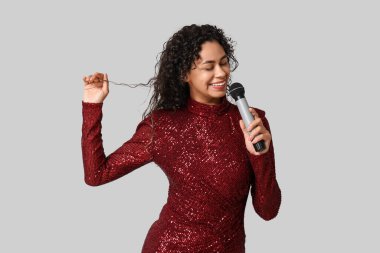 Beautiful young happy African-American female singer with microphone singing on grey background