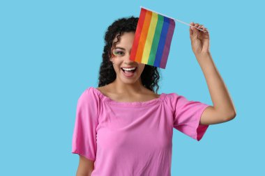 Mavi arka planda gökkuşağı bayrağı olan mutlu Afro-Amerikalı kadın. LGBT kavramı