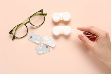 Cımbız, gözlük ve kontakt lensler için bej arka planda bulunan kadın eli.