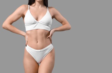 Gri arka planda beyaz iç çamaşırlı genç bir kadın.