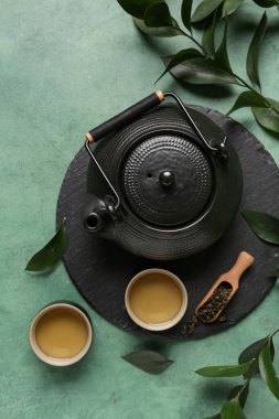 Fincanlı çaydanlık, bir kepçe kuru çay ve yeşil grunge arka planda yapraklar