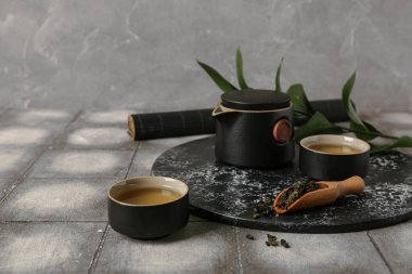 Fincanlı çaydanlık, bir kepçe kuru çay ve gri grunge arka planına karşı fayans masasında yapraklar