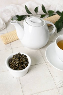 Çaydanlık ve kase, beyaz fayanslı kuru çay yaprakları.