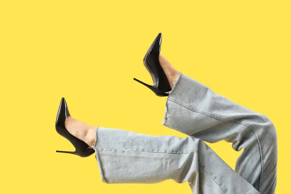 Legs of young woman in stylish black high heels on yellow background