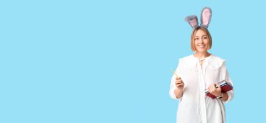 Paskalya tavşanı kulaklı ve mavi arka planda not defteri olan genç bir iş kadını.