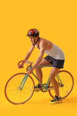 Sarı arka planda bisiklete binen genç erkek bisikletçi
