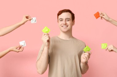 Pembe arka planda prezervatifli genç adam ve eller. Güvenli seks konsepti