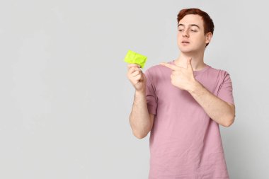 Gri arka plandaki prezervatifleri gösteren genç bir adam. Güvenli seks konsepti