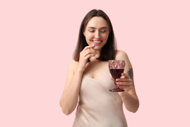 Pembe arka planda kırmızı şarap kadehi olan güzel genç bir kadın.