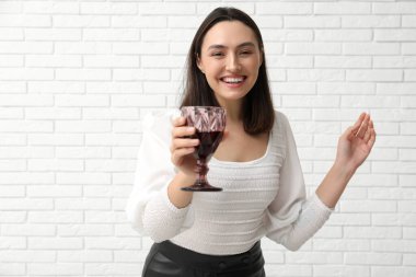 Beyaz tuğlalı arka planda kırmızı şarap kadehi olan güzel genç bir kadın.
