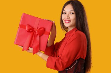 Sarı arka planda hediye kutusu olan güzel bir Asyalı kadın.
