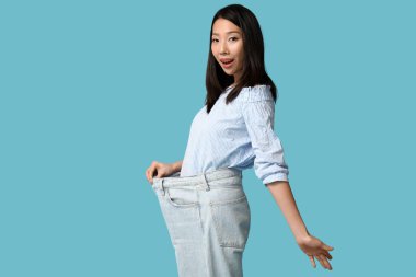 Mavi arka planda bol kotlu güzel, genç, şok olmuş Asyalı kadın.