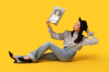 Şık kotlu, dergisi sarı arka planda oturan güzel Asyalı kadın.