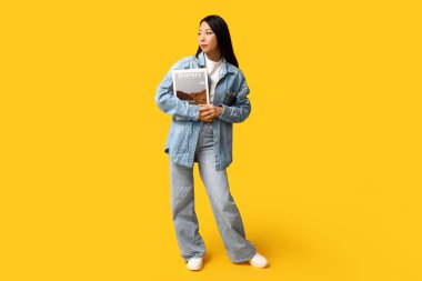 Sarı arka planda şık kot elbiseli güzel Asyalı kadın.