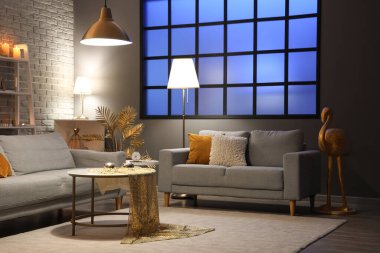 Şık oturma odasının içinde altın dekorlu, geceleri parlayan lambalar ve kanepeler.