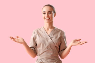 Pembe arka planda bir şey gösteren kadın masaj terapistinin portresi.