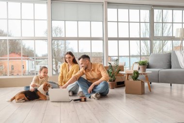 Taşınırken odada dizüstü bilgisayar kullanan Beagle köpekli mutlu bir aile.