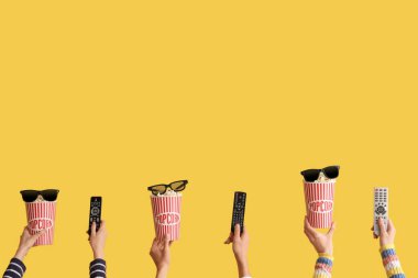 Kovalarca patlamış mısır, televizyon kumandası ve sarı arka planda 3D gözlüklü bir sürü el.