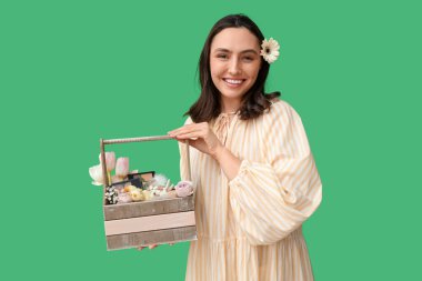 Yeşil arka planda dekoratif kozmetik ürünleri olan Paskalya sepeti tutan güzel genç bir kadın.