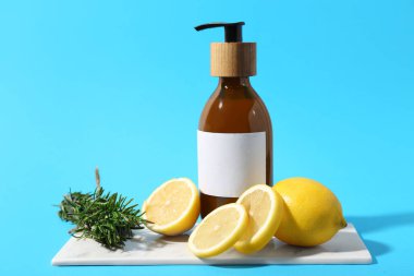 Kozmetik ürünler şişesi, taze limon ve biberiye renkli arka planda.