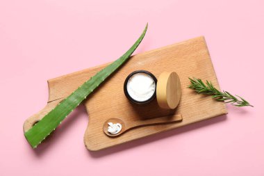 Ahşap tahta tahta bir kavanoz kozmetik ürünü, aloe vera ve pembe arka planda biberiye.