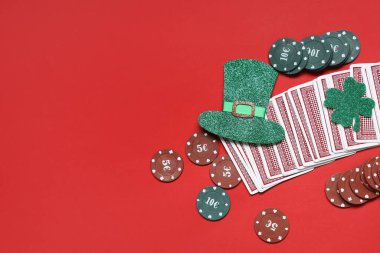 Poker fişleri, kartlar, leprikon şapka ve kırmızı arka planda şanslı yonca. Aziz Patrick Günü kutlaması