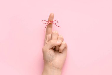 Pembe arka planda işaret parmağında kırmızı fiyonk olan bir kadın el. Hatırlatma konsepti