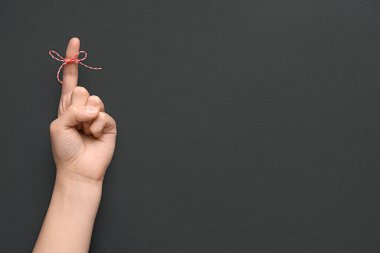 İşaret parmağında kırmızı fiyonklu kadın eli siyah arka planda. Hatırlatma konsepti