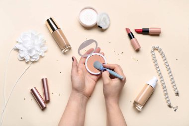 Bej arka planda farklı dekoratif kozmetik ve takılara sahip kadın elleri