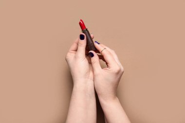 Kahverengi arka planda kırmızı ruj olan kadın elleri.