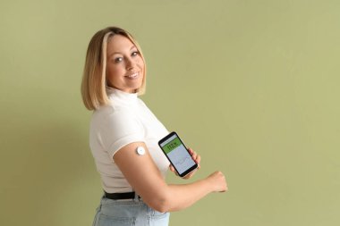 Glikoz sensörü olan şeker hastası bir kadın yeşil zemindeki kan şekerini ölçmek için cep telefonu kullanıyor.