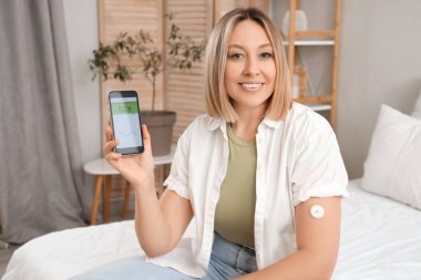 Glikoz sensörü olan şeker hastası bir kadın yatak odasındaki kan şekerini ölçmek için cep telefonu kullanıyor.