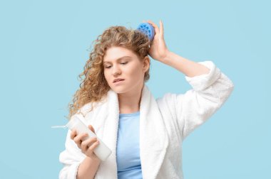 Güzel genç bir kadın mavi arka planda bir şişe şampuanla saç derisi masajı yapıyor.