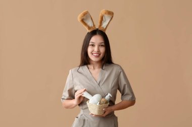 Tavşan kulaklı Asyalı kadın masaj terapisti ve kahverengi arka planda banyo malzemeleri. Paskalya kutlaması