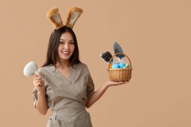 Tavşan kulaklı kadın Asyalı masaj terapisti. Bitkisel çanta ve kahverengi arka planda Paskalya yumurtası.