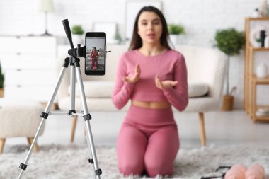 Kadın spor blogcusu evdeki cep telefonunun ekranında video kaydediyor.