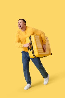 Sarı arka planda bavulla koşan erkek turist.