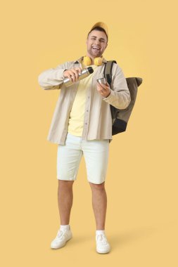 Sırt çantası ve sarı arka planda termosu olan erkek turist.