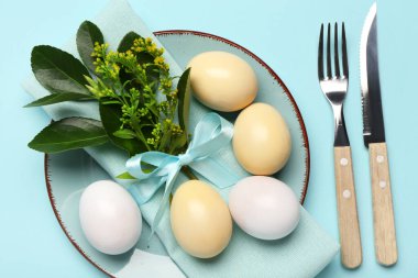 Mavi arka planda Paskalya yumurtaları, peçete ve çatal bıçak seti olan güzel bir masa.