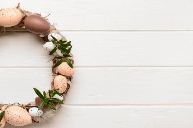 Beyaz ahşap masada yumurta ve çiçeklerle süslenmiş güzel Paskalya çelengi. Üst görünüm