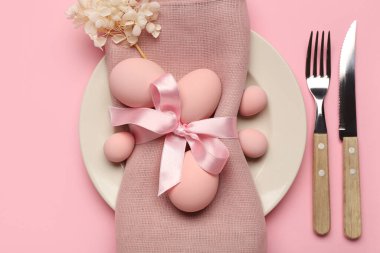 Paskalya yumurtaları, peçete ve pembe arka planda çatal bıçak seti olan şık bir masa.