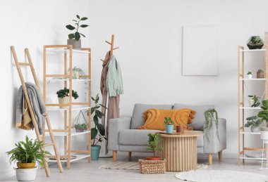 Raflarla, ev bitkileriyle, masa ve kanepelerle dolu rahat bir oturma odası.