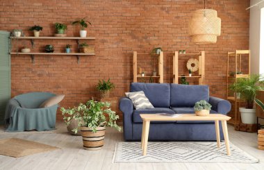 Oturma odasının içinde kanepe, raf üniteleri, puf, masa ve ev bitkileri var.